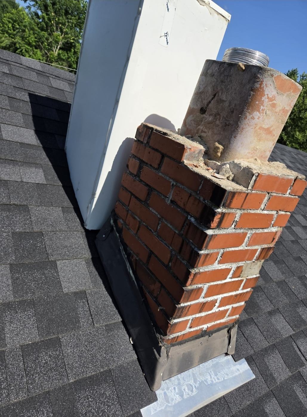 Chimney with the crown broken off and the top courses of brick coming apart, clay flue tile and metal liner left standing exposed