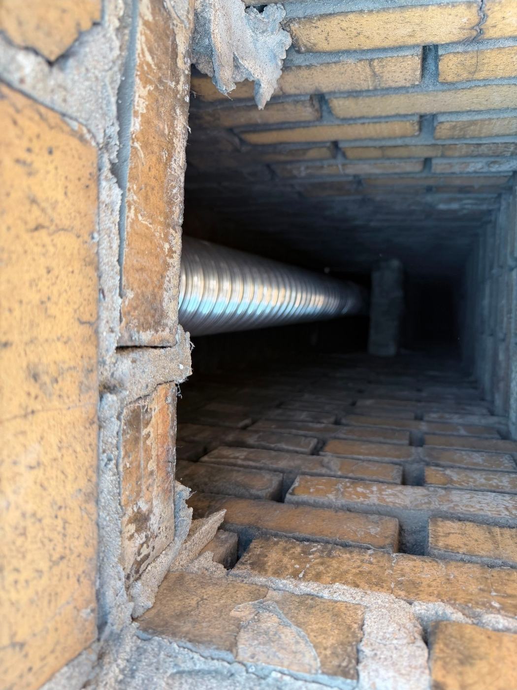 Looking down a masonry chimney flue from the roof at a new stainless liner running the full height inside the old flue