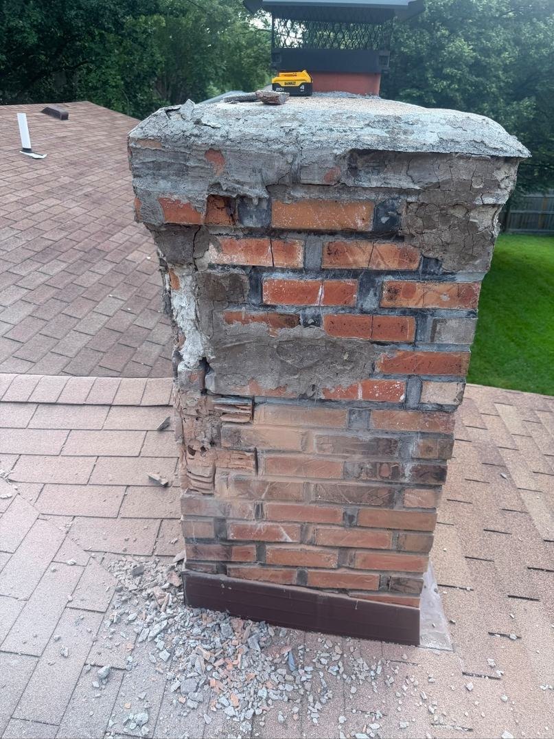 Spalled chimney brick above the roofline with mortar smeared over the face as a cosmetic patch instead of a real repair, St. Louis MO