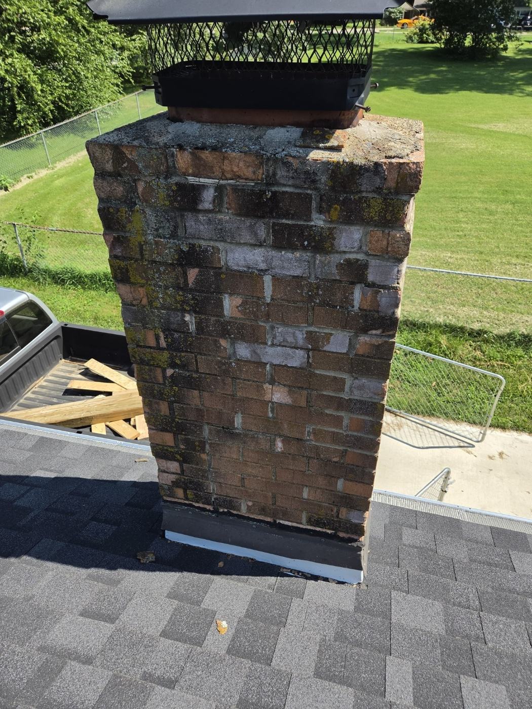 Chimney above the roofline with spalling brick faces, heavy moss and algae and a broken crown, St. Louis MO